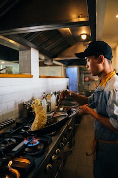 Young chef expertly tossing fried rice in a wok in a bustling restaurant kitchen.