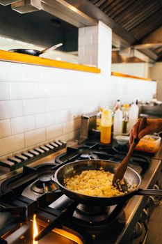 A chef skillfully prepares fried rice in a professional kitchen with a focus on the dish and utensils.
