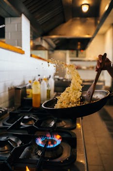 Chef skillfully tossing fried rice in a hot wok over a stove flame in a restaurant kitchen.
