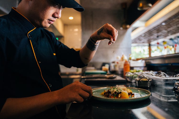 A Chef Sprinkling Sesame Seeds On A Salad Dish