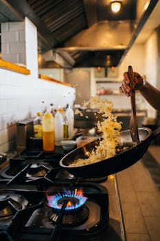 A chef skillfully tosses fried rice in a pan over a flame in a modern restaurant kitchen.