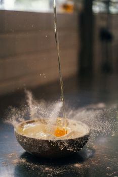 Capturing the moment of an egg being dropped into a flour-filled bowl, creating a splash in a kitchen setting.