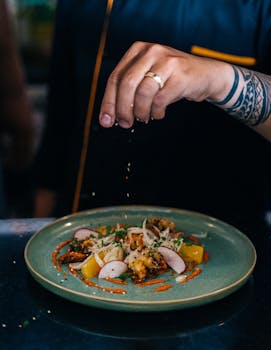 A chef adding final touches to a gourmet dish in an indoor restaurant kitchen.