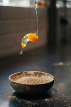 Egg yolk dropping into a flour bowl, capturing the essence of baking preparation.