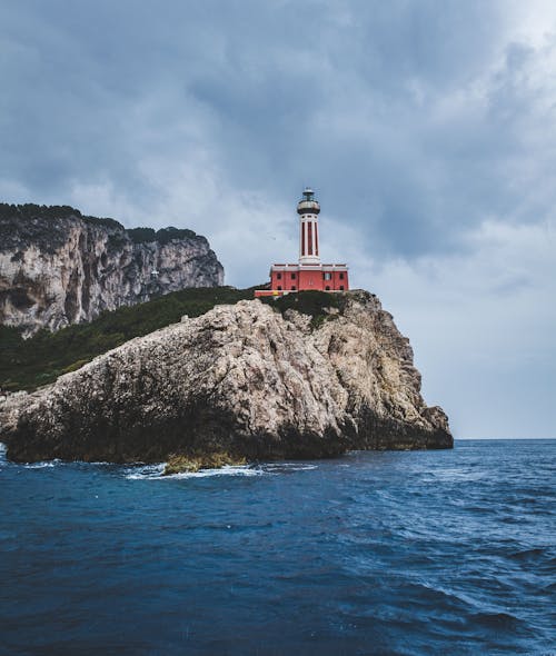 Ücretsiz Deniz Kenarındaki Tepelerin Tepesinde Kırmızı Deniz Feneri Stok Fotoğraflar