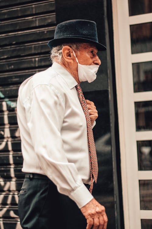 Free Low angle side view of old man in formal wear and protective mask strolling on street Stock Photo