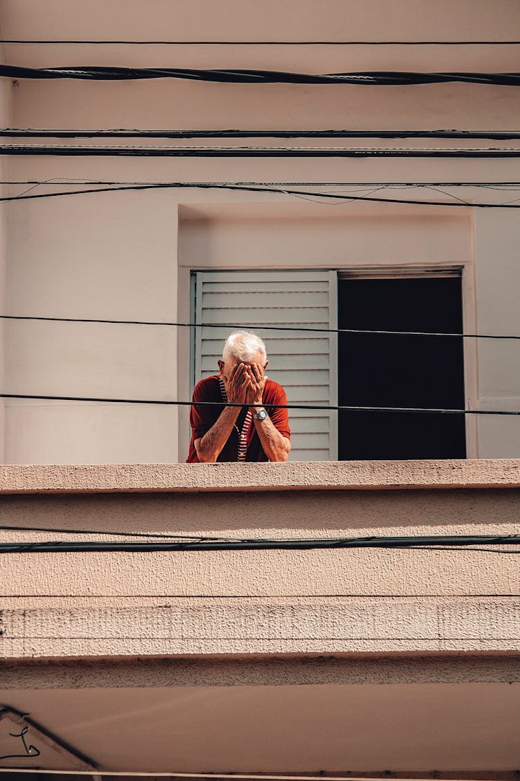 Old Man Standing On Balcony And Covering Face