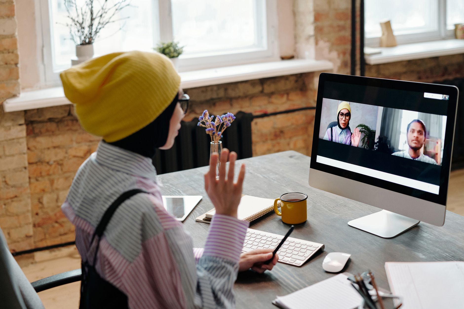 Woman in a yellow beanie on a video call on a computer screen with two other people on webcam