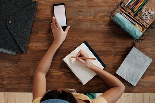 Girl Using Smartphone Writing in Notebook