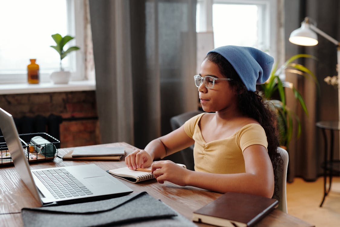 Girl Sitting in Front of a Laptop with Books Open on the Desk 