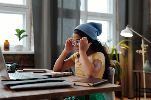 Girl Sitting in Front of a Laptop with Books Open on the Desk 