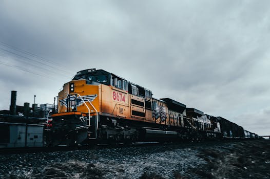Yellow freight train speeding through an industrial area on a cloudy, overcast day.