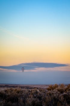A serene landscape with a lighthouse surrounded by mist at sunrise.