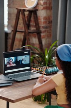 Woman using a laptop for a video call while sitting indoors at a wooden table.