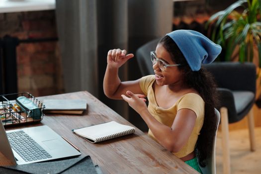 Young girl engaged in an online learning session using a laptop, smiling and taking notes.