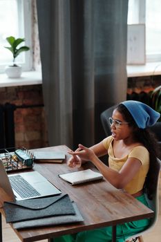 A girl participates in an online class using a laptop at her home desk.