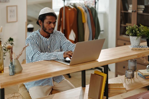 Young man in striped shirt focusing on a laptop while sitting in a modern home office with natural decor.