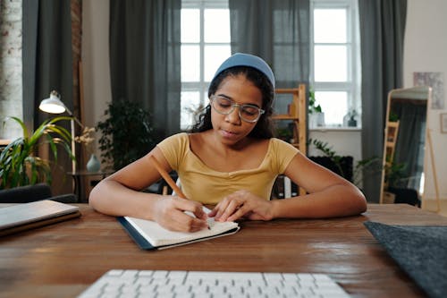Girl Writing in a Notebook in front of a Computer 