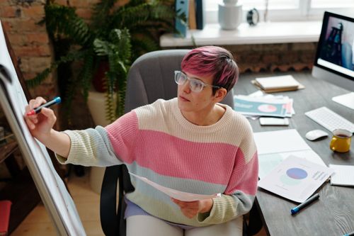Free Woman with colorful hair writing on a flip chart in a modern office setting. Stock Photo