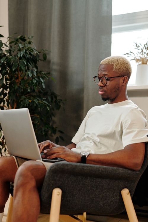 Free African American man with blond hair using laptop while sitting indoors. Stock Photo