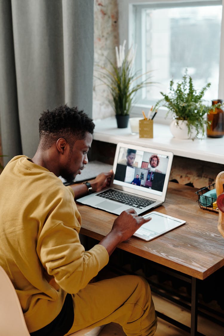 Man In Yellow Long Sleeve Video Calling Using A Laptop