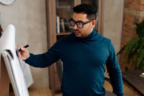 Free Man wearing glasses teaching at home using a whiteboard. Stock Photo