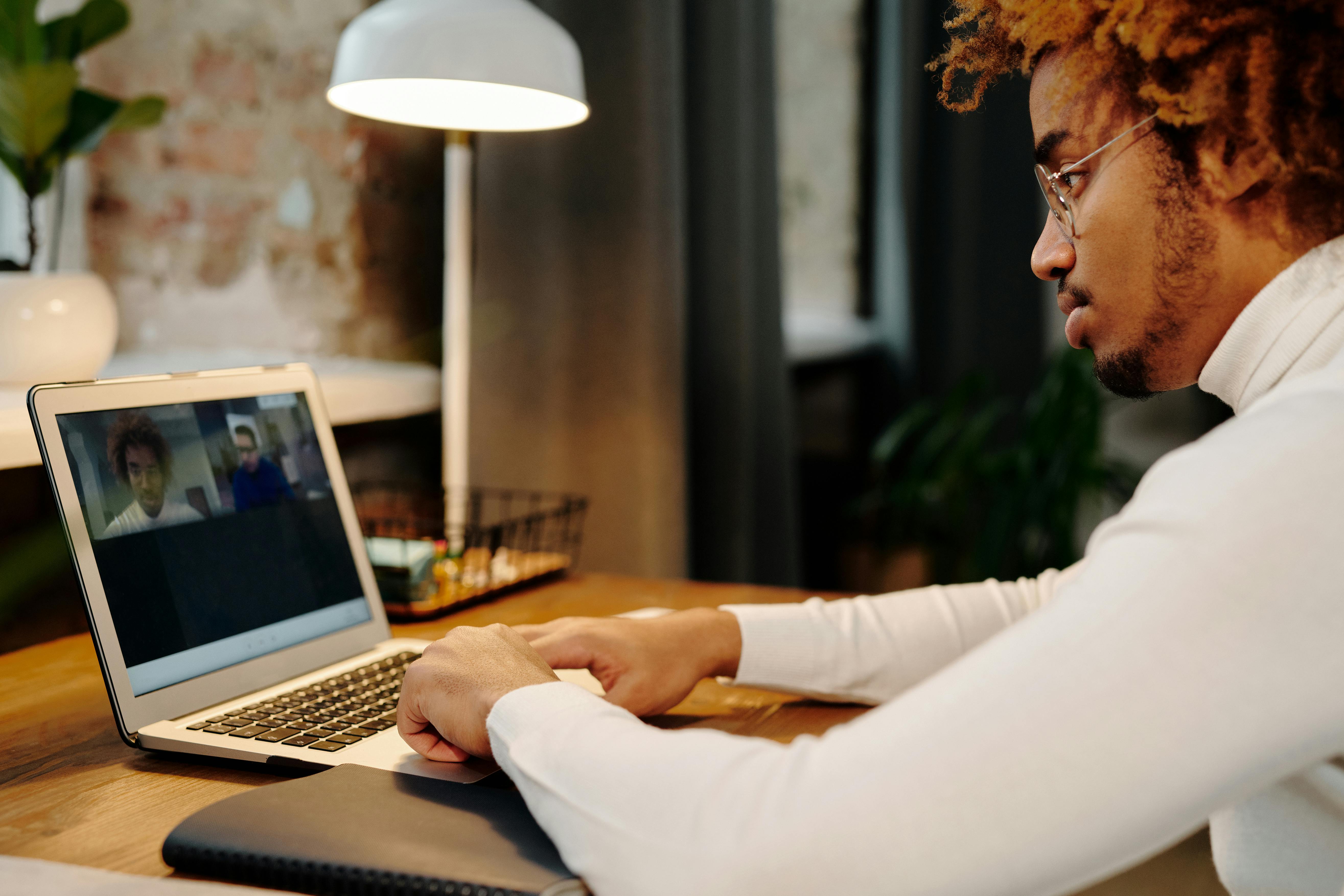 Young man participates in online meeting using a laptop from his home office setup.