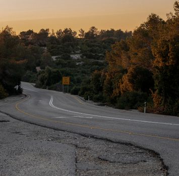 A quiet, winding road in a forested area during sunset, showcasing tranquility and nature's beauty.