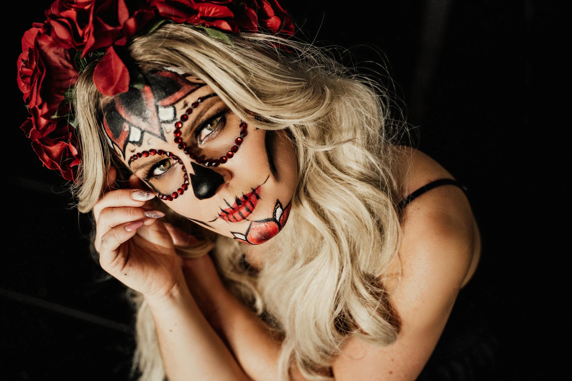 From above of feminine young lady with long blond hair and creative sugar skull makeup ad floral wreath looking at camera during celebration of Mexican Day of the Dead holiday