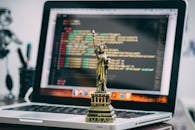 笔记本电脑上放置着一座微型自由女神像，显示着代码，象征着技术自由