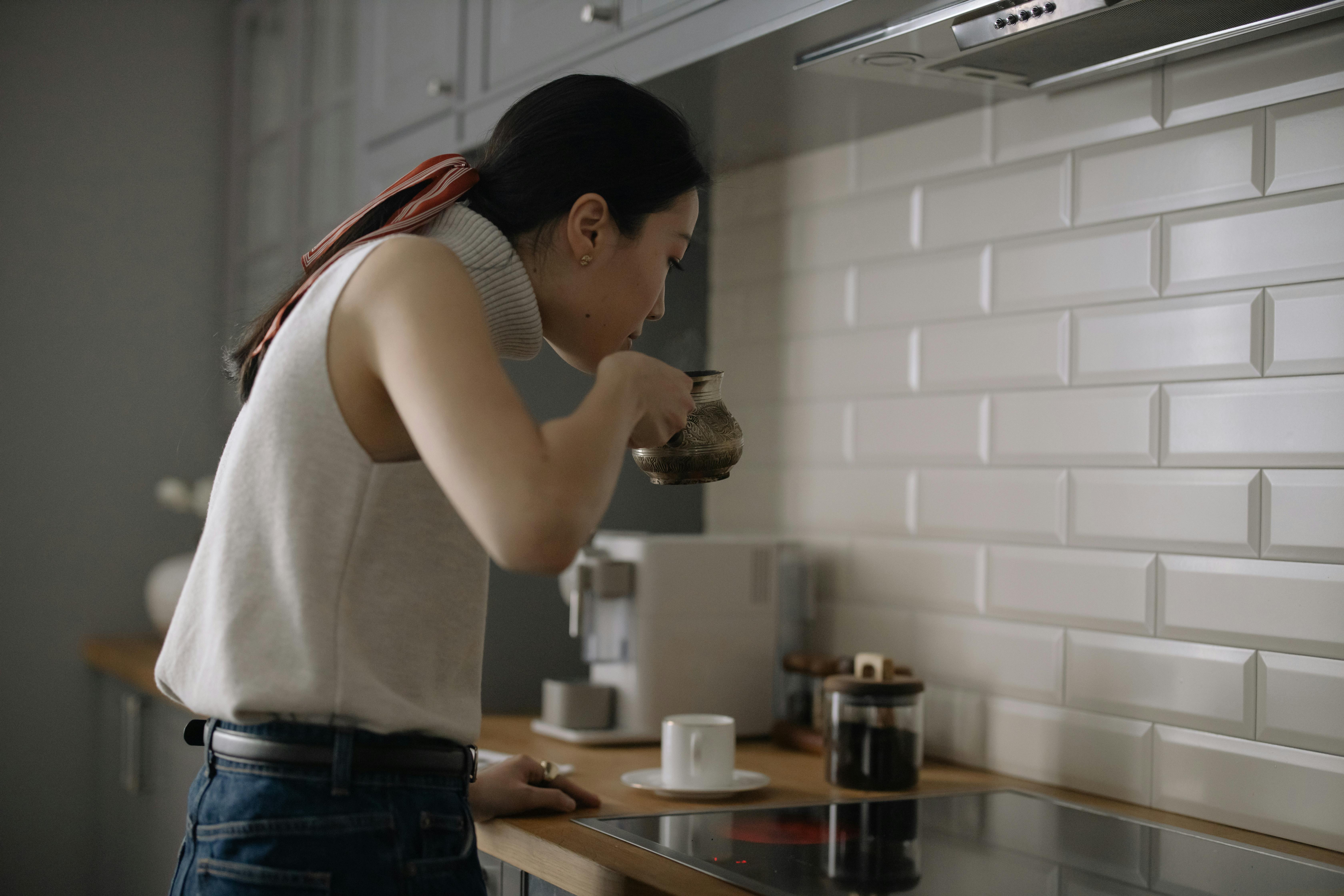 An Asian woman in a modern kitchen carefully preparing coffee in a pot.