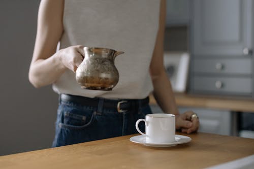A Person Holding a Teapot near a Cup on a Saucer