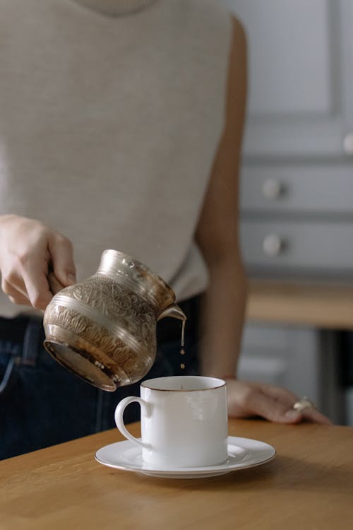 A Person Pouring Hot Drink on a Ceramic Cup