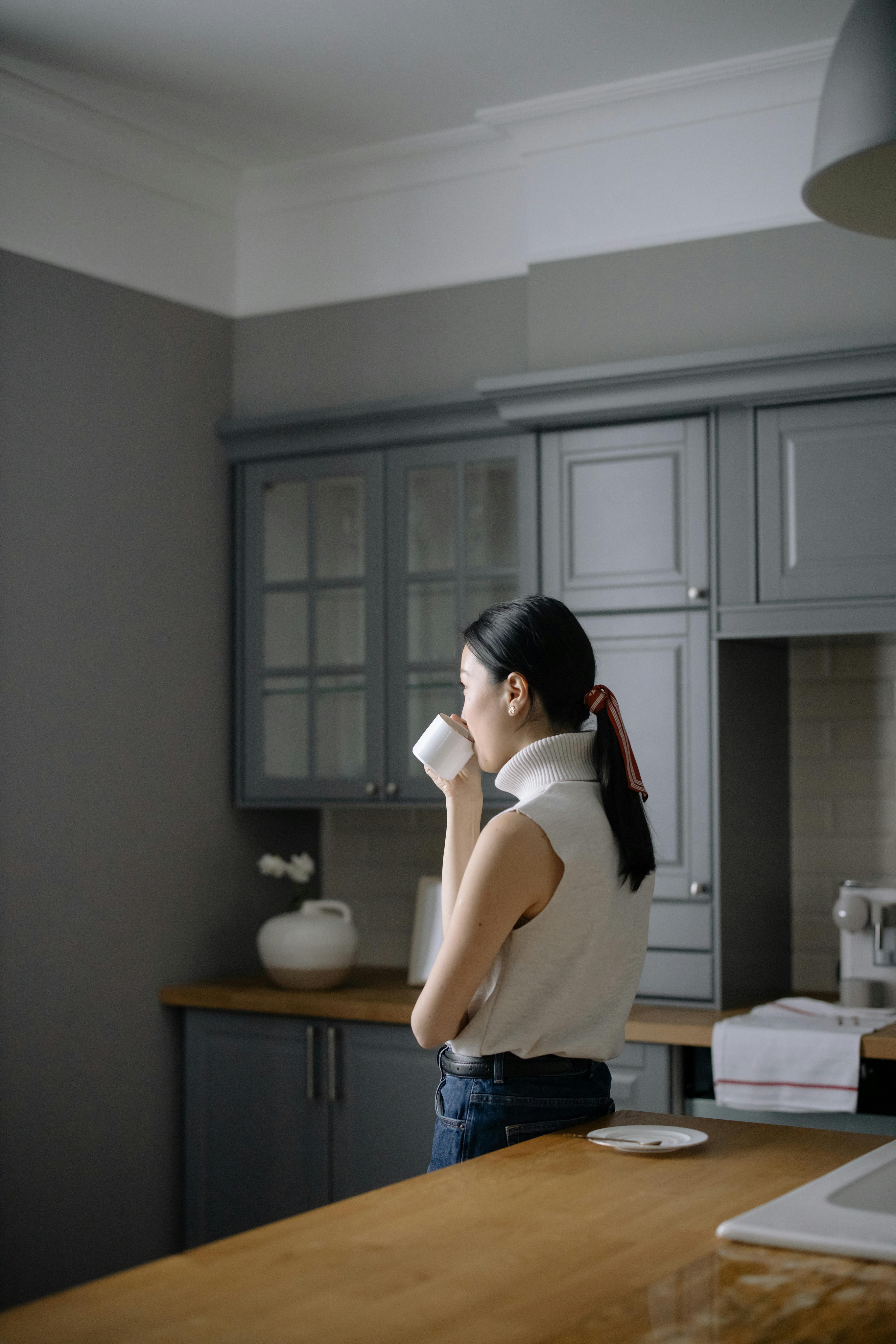 A woman in a sleeveless shirt enjoying a cup of coffee in a stylish kitchen.