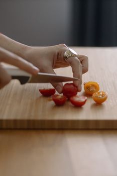 Hand slicing cherry tomatoes on a wooden board with a knife. Perfect for culinary and cooking themes.