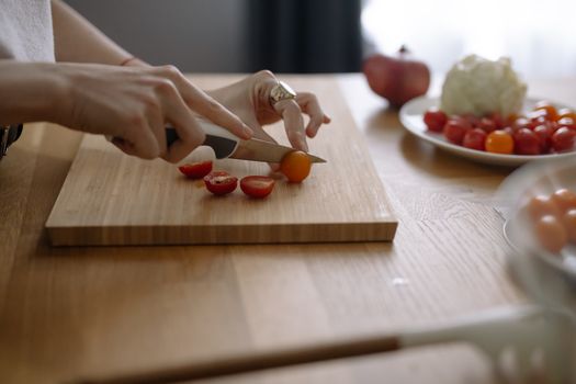 Close-up of hands slicing cherry tomatoes on a wooden chopping board in a kitchen setting.
