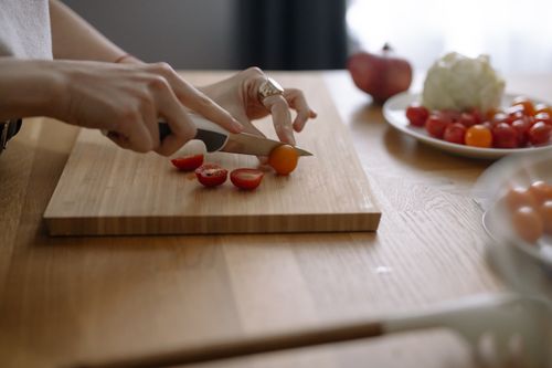 Free Close-up of hands slicing cherry tomatoes on a wooden chopping board in a kitchen setting. Stock Photo