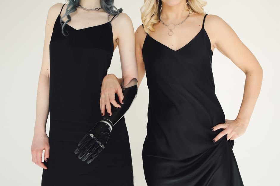 Two fashionable women posing together in black dresses, highlighting friendship and style with a bionic prosthetic arm.