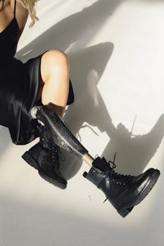 Model with a prosthetic leg in leather boots and black dress showcasing fashion and empowerment.