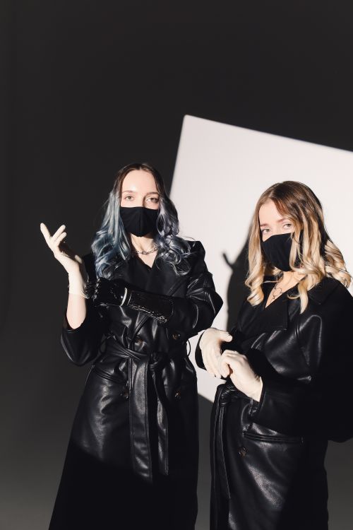 Free Two women with masks in stylish leather coats posing in a modern studio. Stock Photo