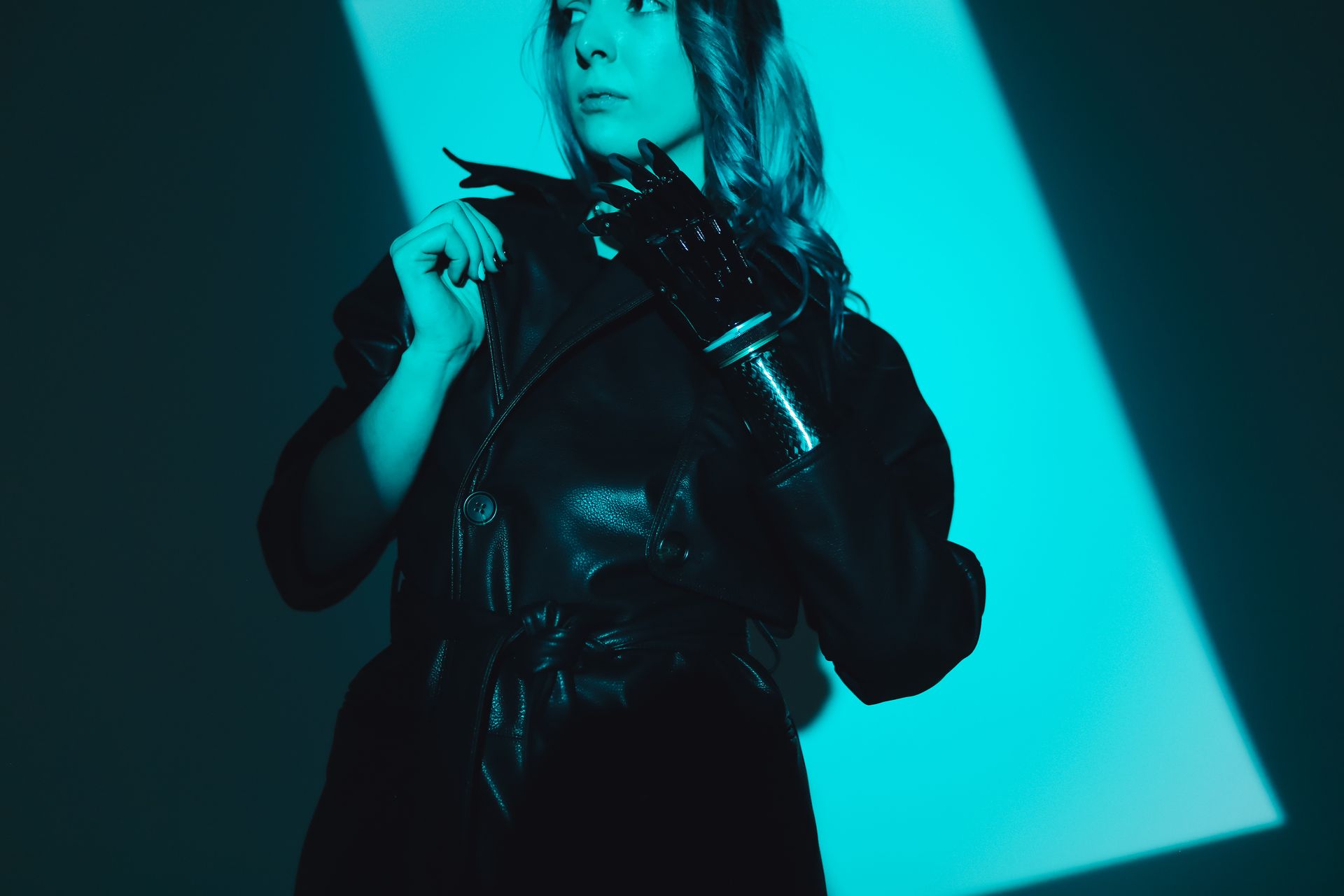 A woman in a leather jacket poses with a prosthetic hand under moody studio lighting.