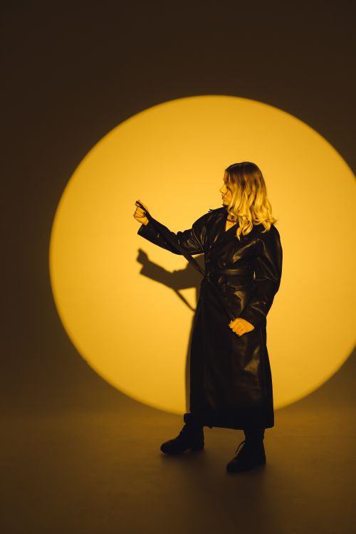 Free Stylish woman in black leather coat posing against dramatic yellow backdrop. Stock Photo