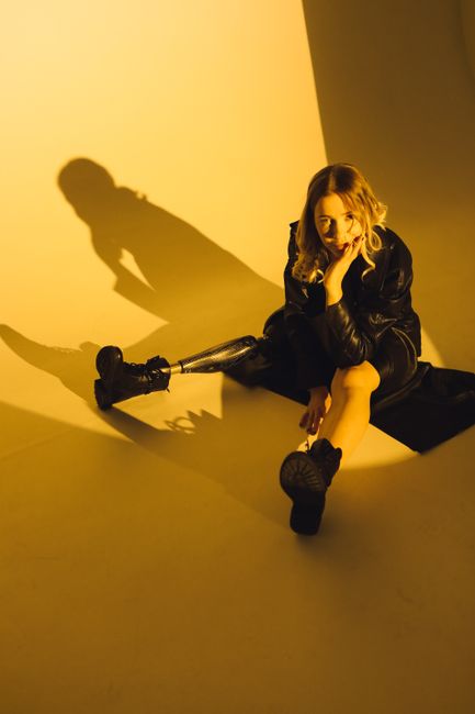 Fashionable woman in black leather showcasing prosthetics in a moody studio setting.