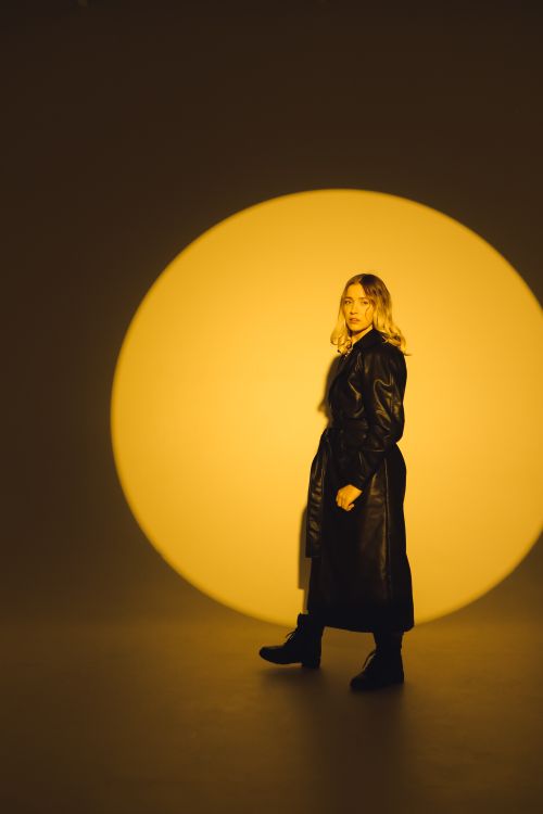 Free Fashionable woman in black leather coat posing with a dramatic yellow spotlight. Stock Photo