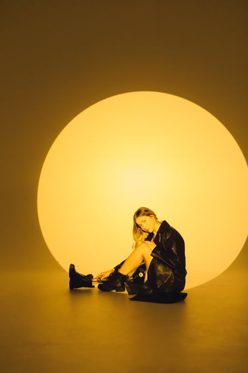 Free Fashionable woman in black leather jacket posing stylishly under a dramatic circular light. Stock Photo