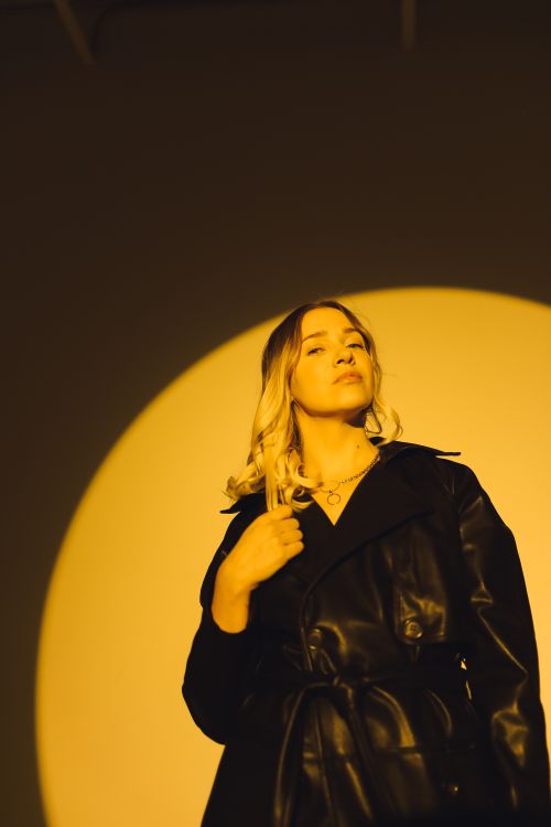 Free A fashionable woman in a black leather jacket poses confidently under dramatic lighting. Stock Photo