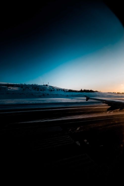 Free View through porthole on wing of airplane taking off from runway on snowy airfield at cloudless winter sunset Stock Photo