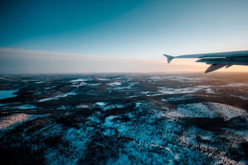 Aircraft flying over vast endless valley covered with forest and snow under sunset sky in evening