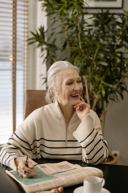 Smiling elderly woman solving crossword puzzle at home, enjoying a quiet indoor moment.