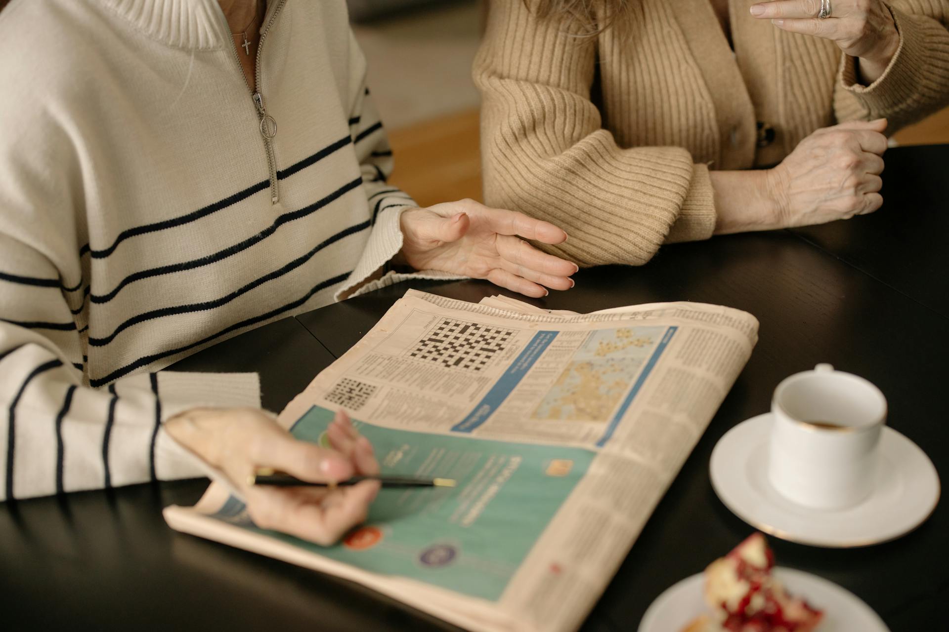 Elderly women discussing a newspaper crossword while enjoying coffee indoors.